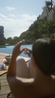 Bir kadın havuz başında güneşli bir sabah geçirir. Kahvaltı masasında, denize bakan ve tropikal bir yerde uçurumlar olan..