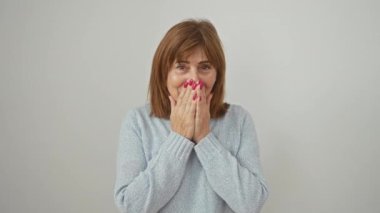 Utangaç orta yaşlı kadın bir skandala karıştı, utancıyla gülüyor. ayakta, eliyle ağız kaplayan; spor kazak, beyaz arka planda izole.