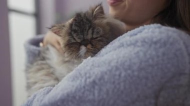 Ev ortamında rahat bir Asyalı kadın, sevgi dolu bir kedi tutuyor, oturma odasında hassas bir an yaşıyor..