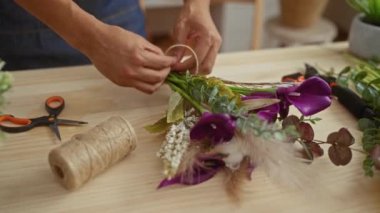 Bir adam bir buket mor zambak ve yeşil yapraklar hazırlıyor. Çiçekçi dükkanında çiçekçilik becerileri sergiliyor..