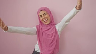 Genç İspanyol kadın tesettür içinde, kolları açık, sevgi dolu bir kucaklaşma için, izole pembe bir tuvale karşı duruyor, mutluluğu ve neşeyi karşılıyor.