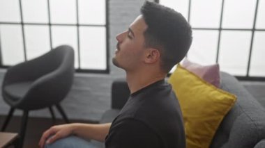 Rahatlamış bir İspanyol genç adam, kanepede uzanıyor, rahat bir ev ortamı sergiliyor..