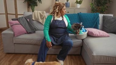 Saçları örgülü genç bir Afrikalı Amerikalı kadın oturma odasında temizlik malzemeleriyle oturuyor ve ayaklarının dibinde bir köpek, rahat ama çalışkan bir ev ortamını yakalıyor..