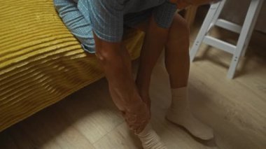Yaşlı bir adam yatak odasında bir yatakta oturuyor, içeride bacağına masaj yapıyor..