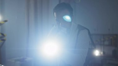 Olgun bir adam, elinde silah ve el feneriyle, kapalı alan ortamında gerilimi ve soruşturmayı sembolize ediyor..