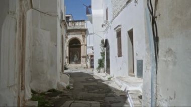 Ostuni 'de dar bir sokak, puglia, italyan, gösterişli beyaz boyalı duvarlar, kırsal binalar ve parlak mavi gökyüzünün altında güzel bir kapı..