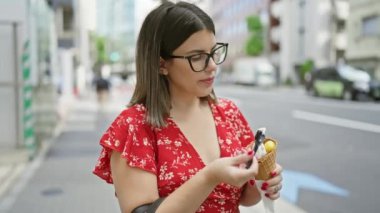 Neşeli, güzel, bardaklı İspanyol bir kadın Tokyo 'nun canlı caddesinde lezzetli bir dondurmanın tadını çıkarıyor. Şehrin şehir mimarisini kucaklıyor. Eğlence dolu yaz tatili gezisi boyunca.