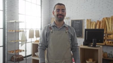 Bıyıklı genç adam gülümsüyor ve pastanede açık tabela tutuyor.