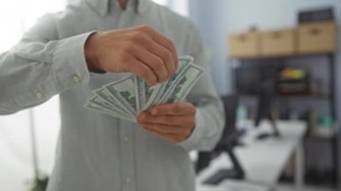 Ofisteki genç adam iki eliyle Amerikan dolarlarını sayıyor, profesyonel bir iş ortamında para idaresine odaklanıyor.