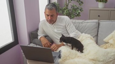 Orta yaşlı İspanyol bir adam evinde Chihuahua köpeğiyle birlikte rahat bir oturma odasında dizüstü bilgisayarıyla çalışıyor..