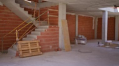Tamamlanmamış bir inşaat alanının bulanık görüntüsü tuğla duvarlar, açık kirişler ve devam eden inşaat sürecini gösteren dağınık materyaller..