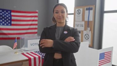 Kollarını kavuşturmuş kendine güvenen genç İspanyol kadın Amerikan bayraklarının önünde bir seçim merkezinde duruyor..