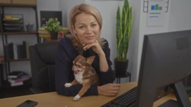 Ofiste çalışan genç, sarışın, beyaz bir kadın kucağında Chihuahua köpeğiyle çalışıyor. Etrafı kapalı bitkiler ve ofis malzemeleriyle çevrili..
