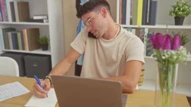 İspanyol bir adam ev ofis ortamında telefon ve laptop ile birden fazla iş yapıyor, konsantre ve profesyonel görünüyor..