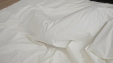 Genç adam rahat bir yatak odasında beyaz çarşaflarla huzur içinde uyuyor.