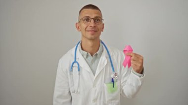 Steteskoplu gururlu beyaz adam pembe kurdele tutuyor, zafer için heyecanlanıyor ve beyaz arka planda izole bir şekilde kollarını kaldırarak başarılı oluyor.