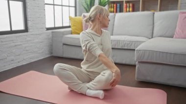 Huzurlu bir kadın modern bir oturma odasında pembe bir paspas üzerinde yoga yapıyor. Huzuru, sağlığı ve yaşam tarzını gösteriyor..