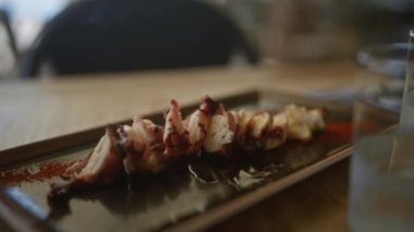 Ahtapot ızgarası, ahşap masa ve bulanık arka planı olan bir açık hava restoranında uzun bir tabakta servis edilir..