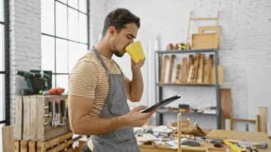 Sakallı, kahve içen ve marangozluk atölyesinde tablet tutan yakışıklı bir İspanyol..
