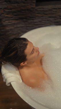 Huzurlu bir kadın lüks bir otelin köpüklü banyosunda rahatlar, sükuneti ve kendine bakımı somutlaştırır..