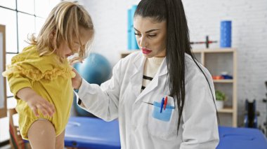 Pediyatrist bir kadın, kapalı bir klinikte küçük bir kızı muayene ediyor..