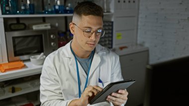 Beyaz laboratuvar önlüklü genç İspanyol adam modern bir laboratuvar ortamında tablet kullanıyor..