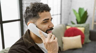 Sabit bir dairede, renkli yastıklı, sabit bir telefonla konuşan yakışıklı bir adam..