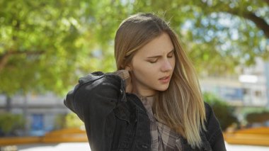 Şehir parkında boynu yeşil boyuna dokunan boynu ağrıyan genç bir kadın..