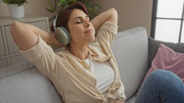 Kısa saçlı güzel bir kadın dinleniyor ve evinin oturma odasında kulaklıkla müzik dinliyor..