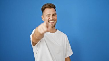 Gülümseyen bir İspanyol kamerayı mavi bir duvarla işaret ediyor..