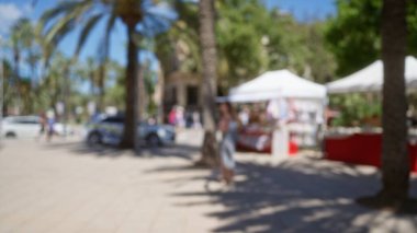 Mallorca vitrininde bulanık bir pazar manzarası. Bulanık palmiye ağaçları, bir kadın, sokak satıcıları, dağılmış insanlar, hareketli market tezgahları ve güneşli bir plaza..