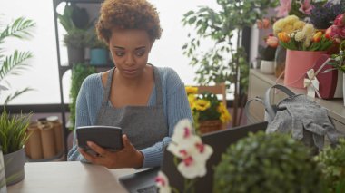 Renkli buketler ve yeşil bitkilerle dolu bir çiçekçide hesap makinesi kullanan Afrikalı kadın..