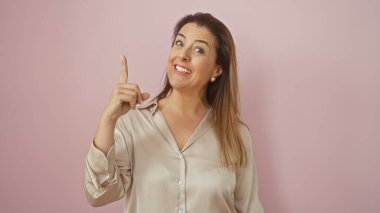 Gülümseyen genç İspanyol kadın yukarıya bakıyor, pembe izole bir arka plana karşı duruyor..