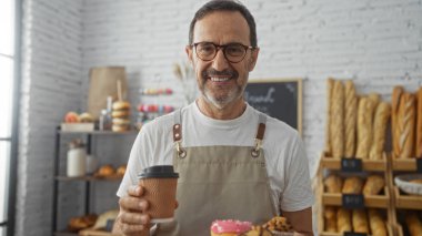 Fırında elinde kahve ve hamur işleri tutan yakışıklı İspanyol bir adam önlük ve gözlük takıyordu..