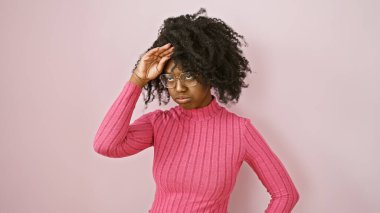 Pembe kazaklı Afro-Amerikan kadın sağlam bir arkaplanda poz veriyor gözlüklü ve doğal saçlı..