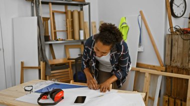 Odaklanmış bir kadın, iyi donanımlı bir marangozluk atölyesinin planlarını inceliyor.