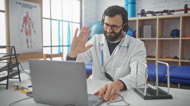 Beyaz önlüklü, sakallı, orta yaşlı bir erkek doktor klinikte tele sağlık danışmanlığı yapıyor..