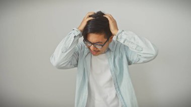 Stresli, gözlüklü, başını beyaz bir arka plana yaslayan Asyalı bir adam..