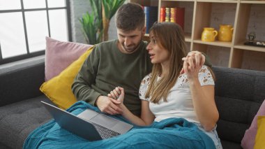 Bir erkek ve bir kadın, modern oturma odasındaki bir dizüstü bilgisayarla rahat bir şekilde kanepede etkileşime girer..