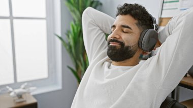 Sakallı gevşek İspanyol adam ofiste kulaklıkla müzik dinlemekten hoşlanıyor.