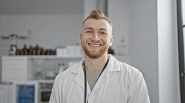 Modern bir laboratuvarda duran, sakallı, laboratuvar önlüğü giyen, gülümseyen beyaz bir adam..