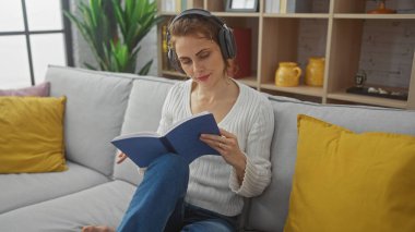 Günlük kıyafetli genç bir kadın, kulaklıkla müzik dinlerken kitap okumaktan, kanepede uzanmaktan hoşlanır..