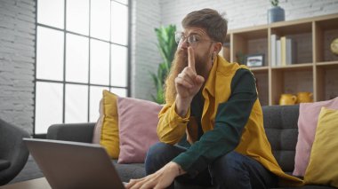 Gözlüklü sakallı genç bir adam içeride sessiz bir jest yapıyor.