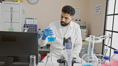 Genç bir adam laboratuvar ortamında bir matarayı inceliyor. Sakalını ve profesyonel davranışlarını gösteriyor..