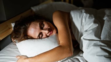 Huzurlu genç bir kadın sıcak ışıkla aydınlatılmış rahat bir yatak odasında rahat bir şekilde uyuyor..