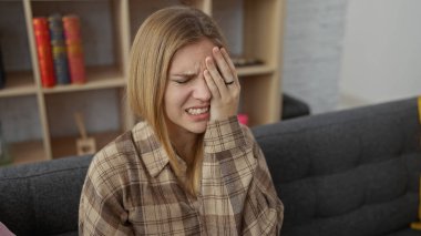 Modern bir oturma odasında göz ağrısı çeken beyaz bir kadın..