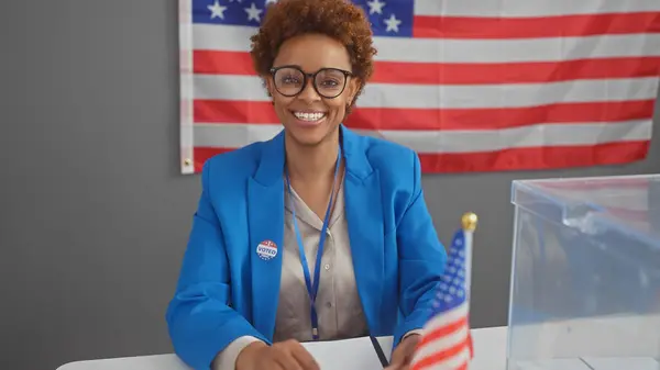 stock image Smiling african american woman with glasses in blue blazer at electoral college with us flag.