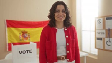Genç, çekici İspanyol bir kadın, arka planında İspanyol bayrağı ve oy sandığıyla İspanya 'daki bir üniversite odasına gülümserken kamerayı işaret ediyor..