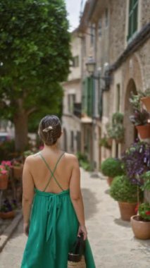 Valldemossa 'da, Mallorca' da, İspanya 'da canlı bitkiler ve büyüleyici evlerle çevrili güzel bir caddede yürüyen bir kadın..