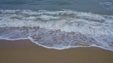 Rahatlatıcı bir kumsal sahnesi. Dalgalar yavaşça kumlu sahile çarpıyor. Doğanın ve huzurlu sahil ortamının özünü yakalıyor..